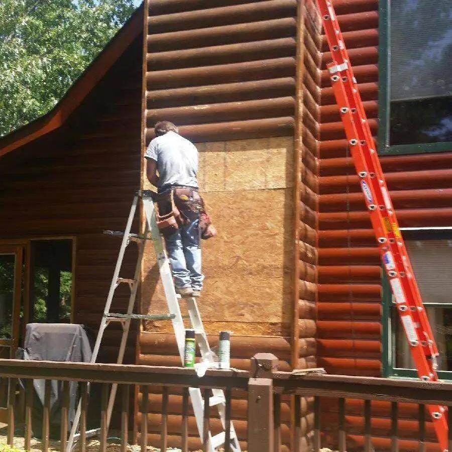 Worker on a ladder replacing a section of log siding